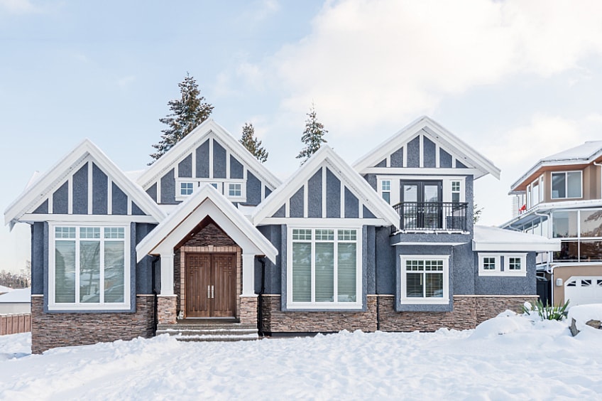 A stone and stucco house covered in snow at wintertime
