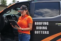 A roofing business owner standing outside of her company vehicle reviewing roofing quotes.