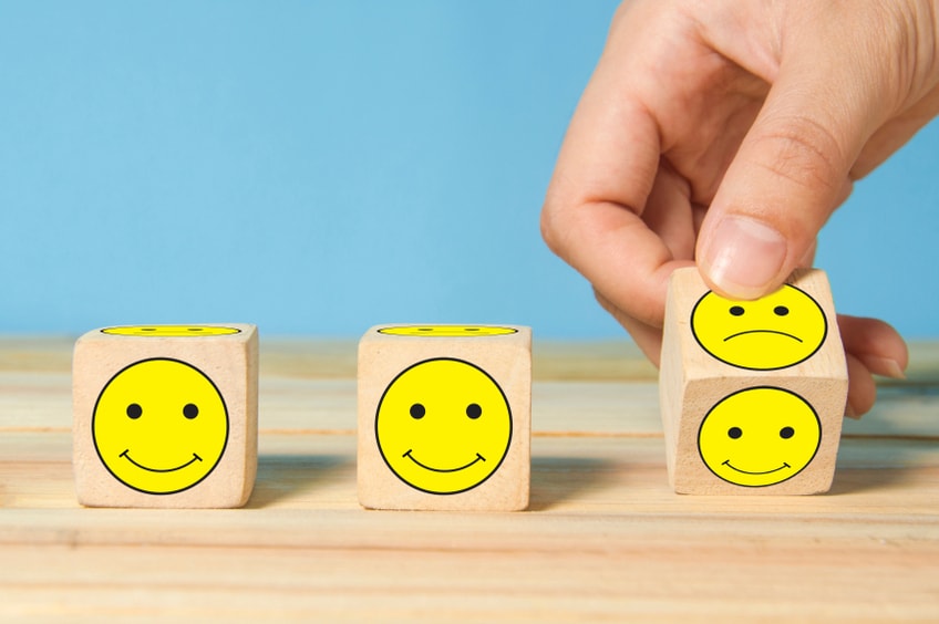 A hand flipping small blocks from sad to smiley faces