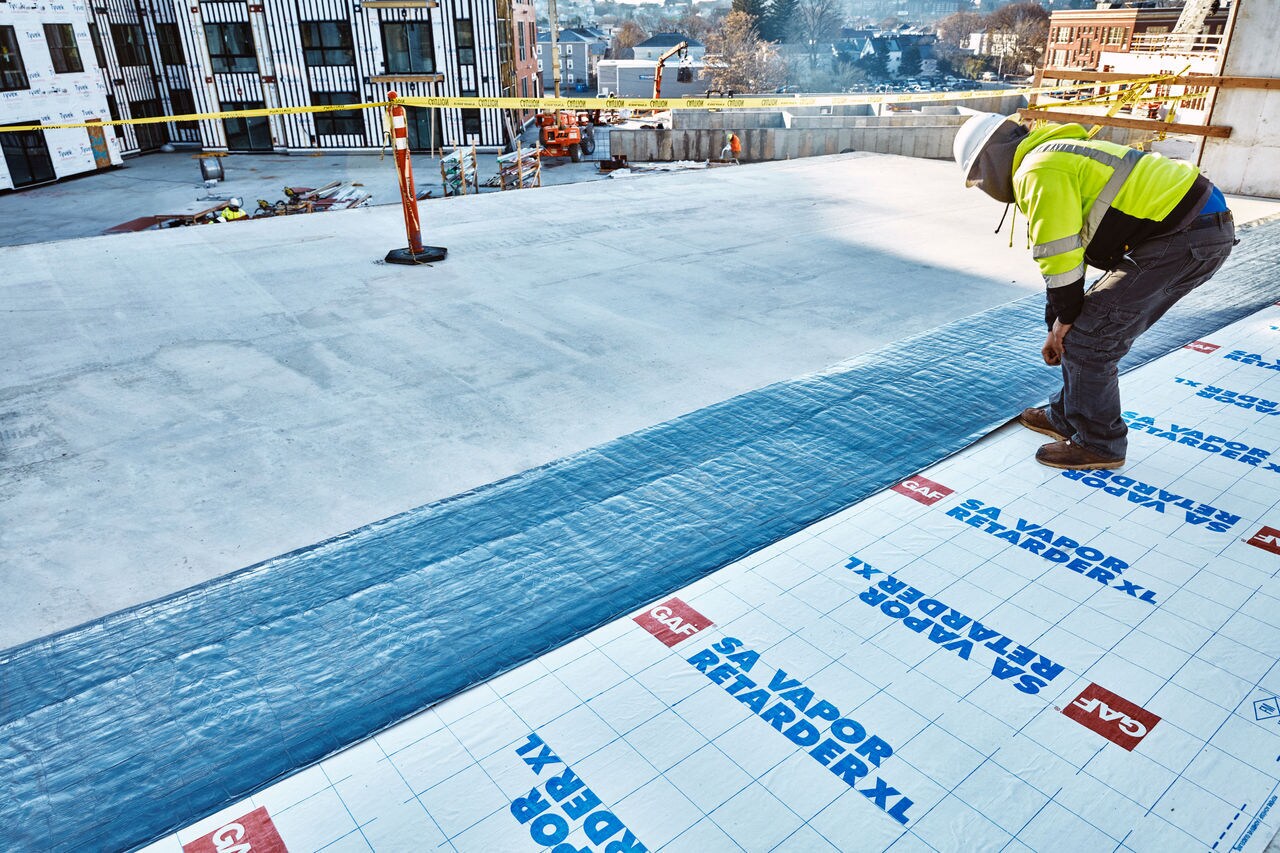 A roofer installing GAF SA Vapor Retarder XL on a roof
