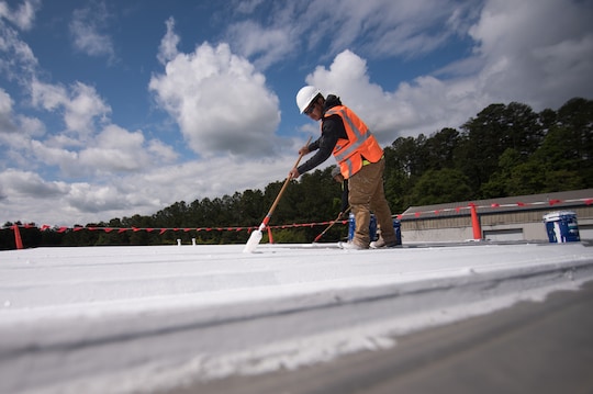 Man in orange vest using roof coating