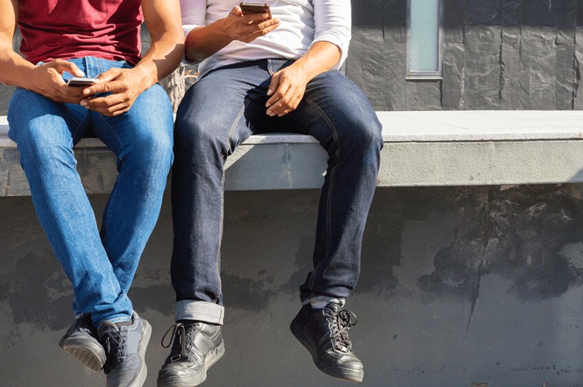Two men on a parapet looking at their phones