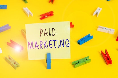 Paid marketing on a sticky note with colorful paper clips on a bright yellow background