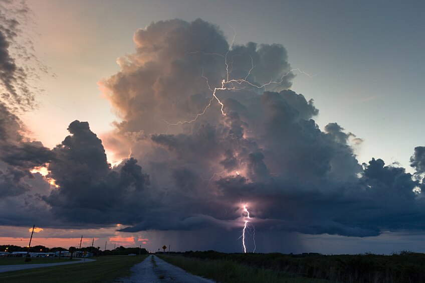 Large lightning storm clouds over a road and a field