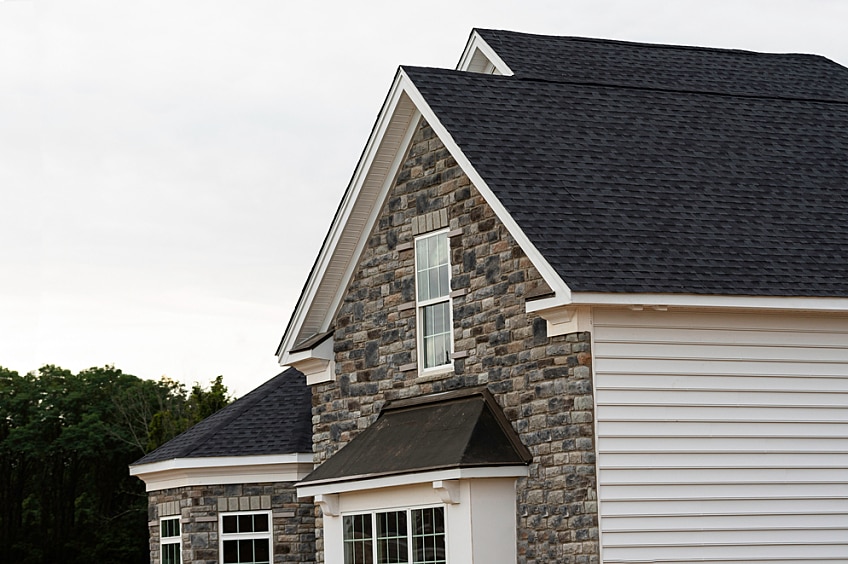 A homeowner compares two shingles in front of a house.