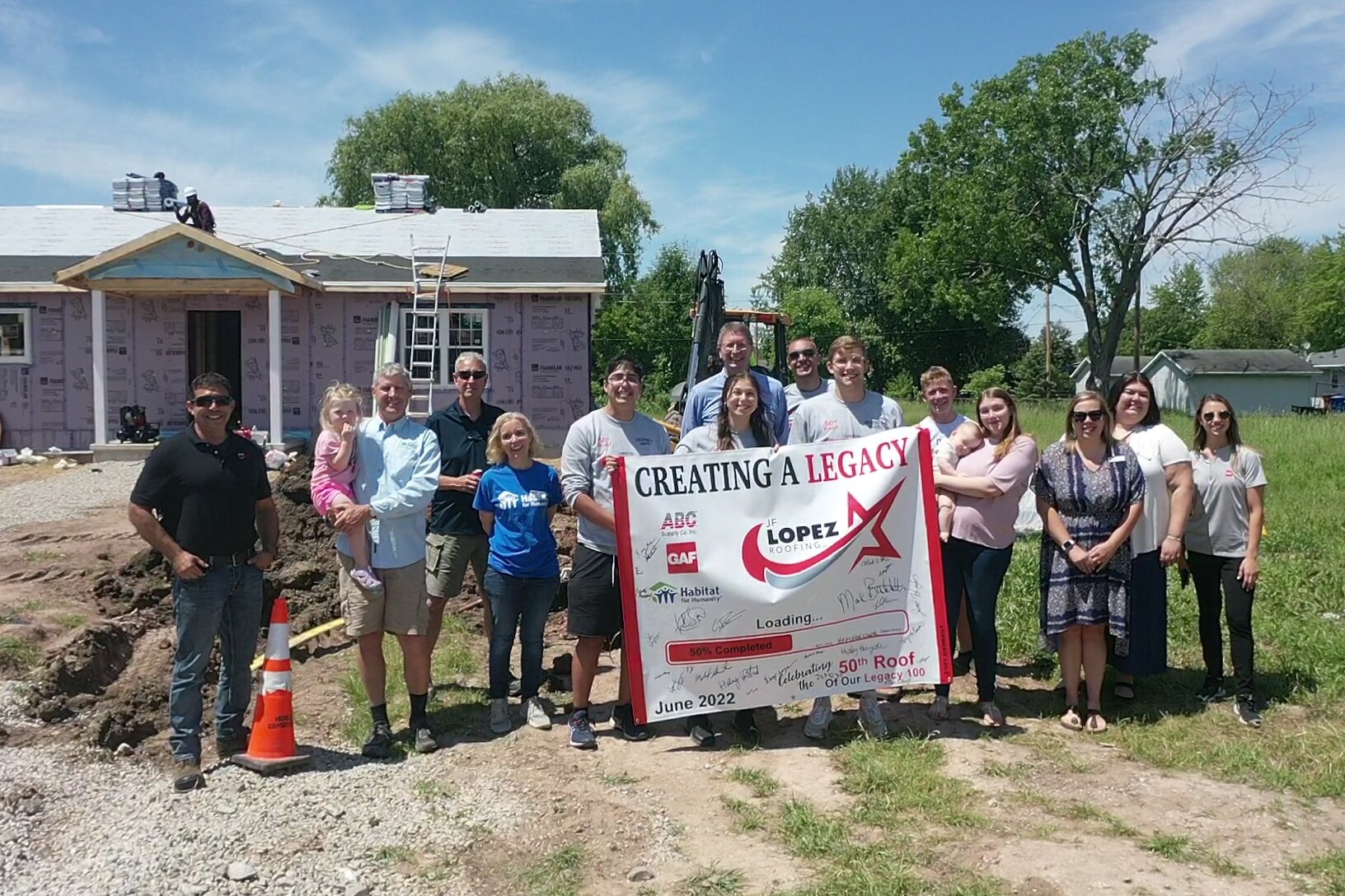 Group of people standing in front of new construction holding a sign reading, "creating a legacy."