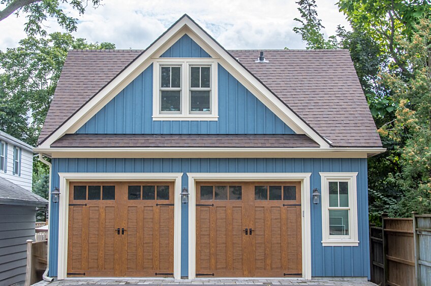 A large vintage retro detached two car cape cod blue style garage, with grey shingled roof, windows,