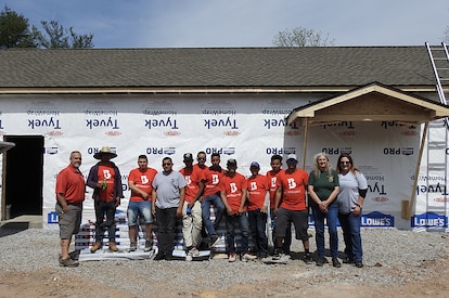 A group of people stand in front of a building on a construction site smiling at the camera.