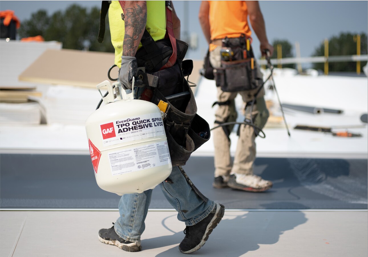 Roofers install GAF EverGuard® TPO Quick-Spray Adhesive on a flat roof