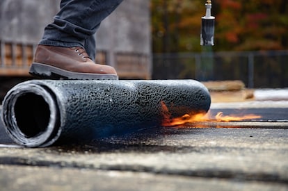 A worker uses a torch to prepare a roofing membrane for installation.