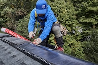 Roofer installing GAF TimberTex ridge cap shingles on the roof of a house.