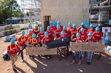 Volunteers in GAF Community Matters shirts stand in front of a home build site.