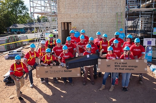 Volunteers in GAF Community Matters shirts stand in front of a home build site.