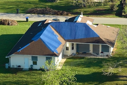 Hurricane Ian damaged house rooftop covered with protective plastic tarp against rain water leaking 