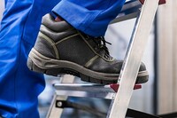 A person wearing roofing shoes while climbing a ladder.