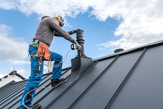 A roofing contractor installs a chimney cricket using a drill.