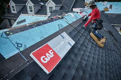 A roofing contractor replaces shingles on a residential roof.