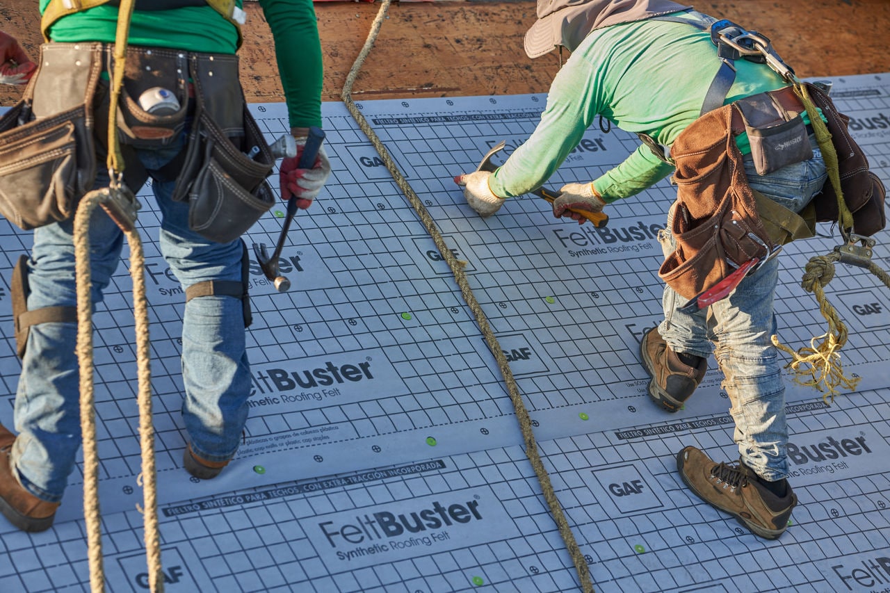 Roofing contractors certified by GAF installing roof materials tied to roof with a saftey rope.