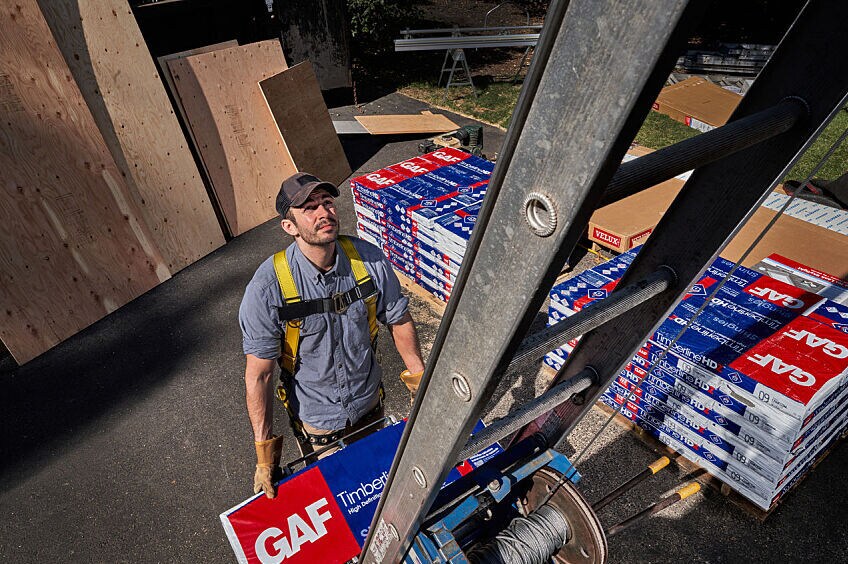 Roofer climbing to second level with GAF shingles using a ladder.