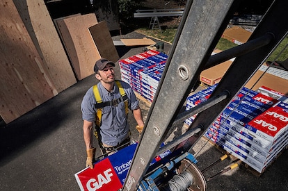 Roofer climbing to second level with GAF shingles using a ladder.