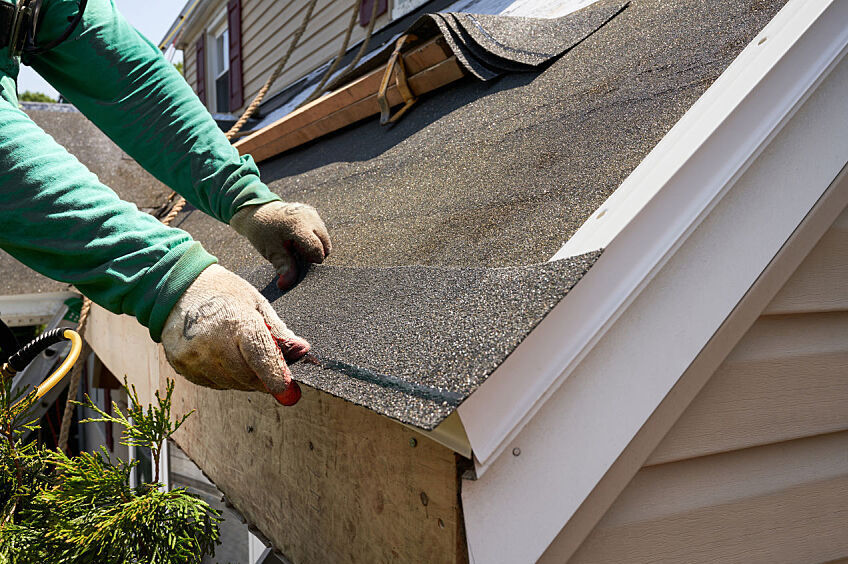 A roofer stands on a ladder and repairs a home's soffit and fascia.