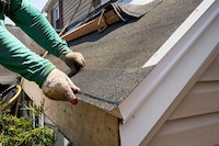 A roofer stands on a ladder and repairs a home's soffit and fascia.