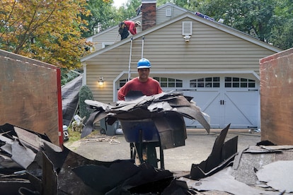 A roofer hauling roofing debris to a dumpster