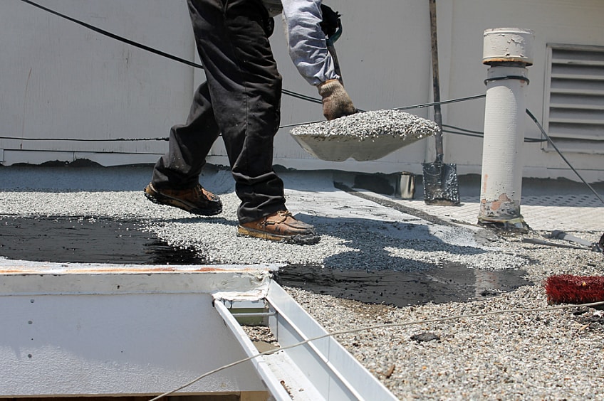 A roofer shovels gravel.