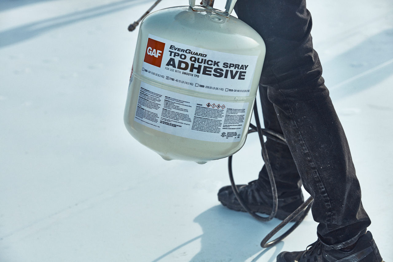 Roofer using EverGuard TPO Quick Spray Adhesive to install TPO on a roof