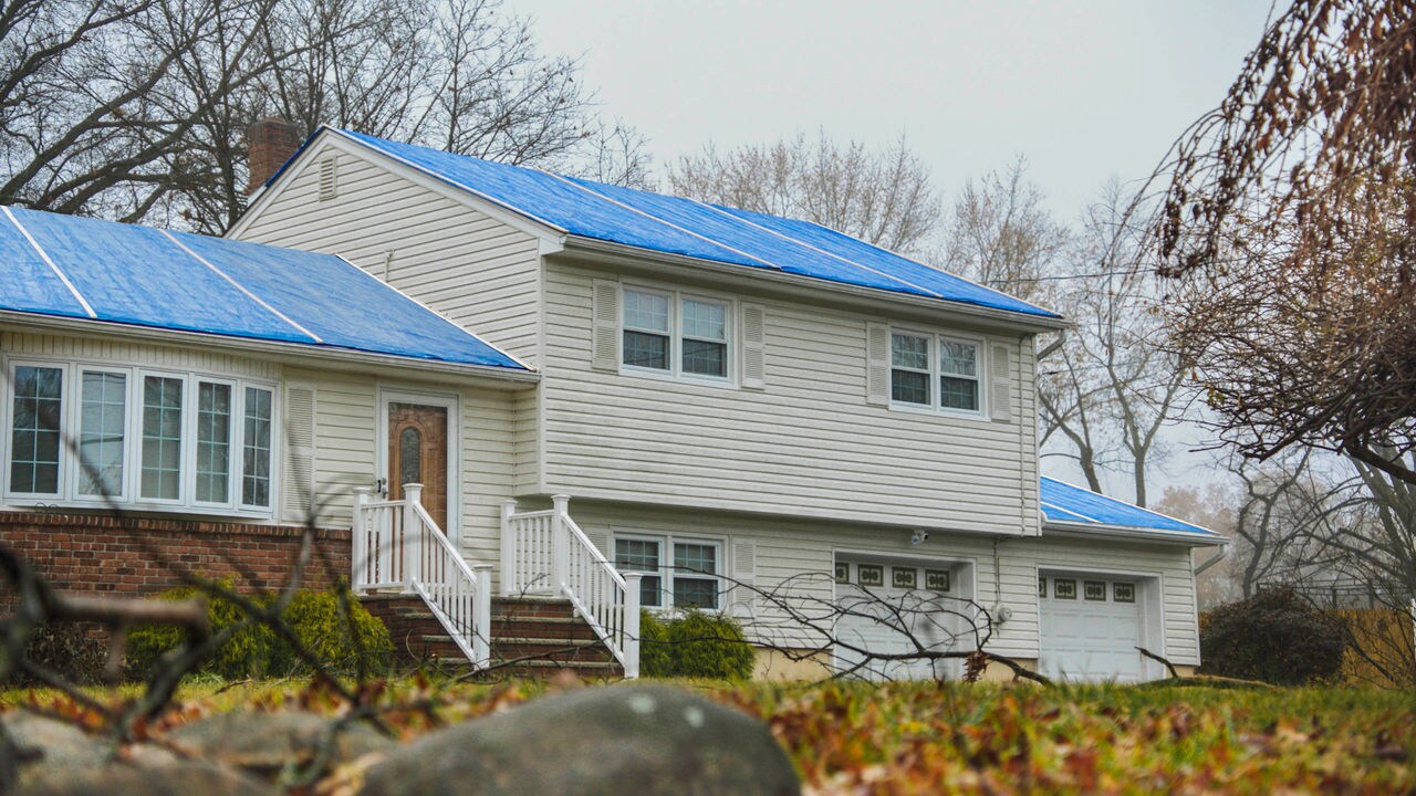 Image of storm-damaged roof with blue tarp on the roof