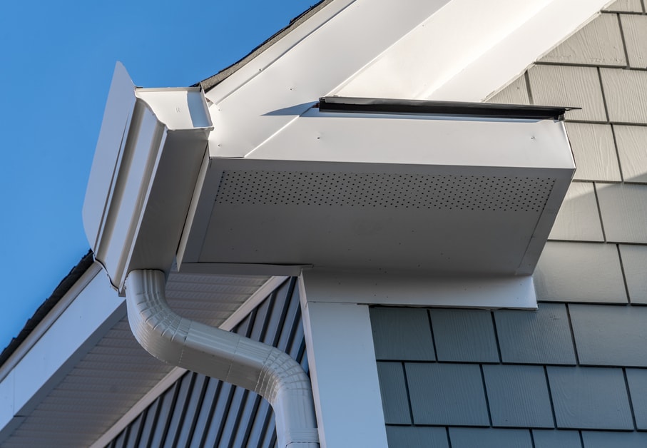 Gutter system that collects water shedding off the roof, with slip connector, end cap, elbow tube, gutter hanger, gutter drop connecting outlet to the downspout, soffit, fascia, gray shingle siding Gutter system that collects water shedding off the roof, with slip connector, end cap, elbow tube, gutter hanger, gutter drop connecting outlet to the downspout, soffit, fascia, gray shingle siding