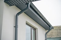 Close-up of a modern home featuring a gray gutter system and window, showcasing sleek architectural 