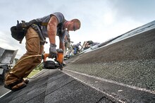 A man with ha nail gun installs shingles