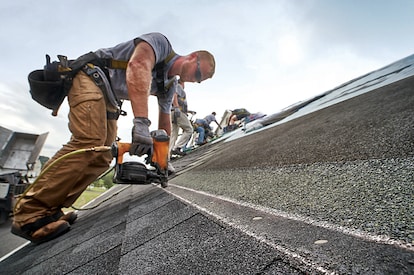 A man with ha nail gun installs shingles