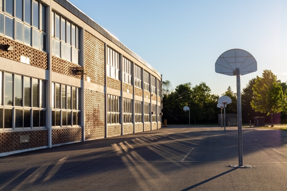Schoolyard with basketball court and school building exterior in the sunny evening.
