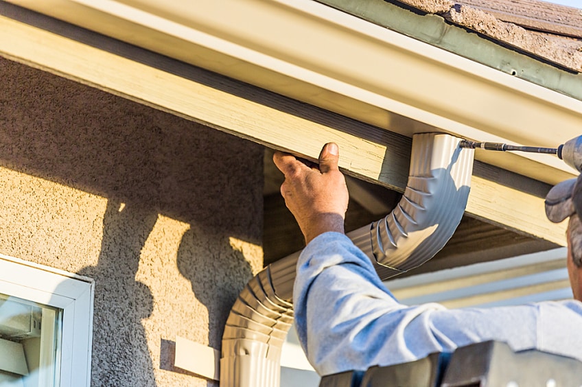 Worker attaches a rain gutter and downspout to a home's fascia.
