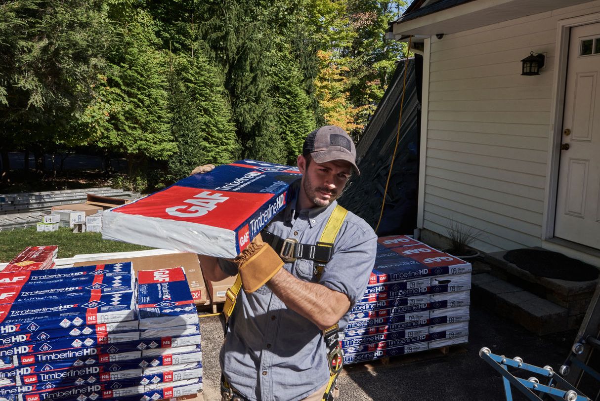 A roofer carries a bundle of GAF Timberline HDZ shingles.