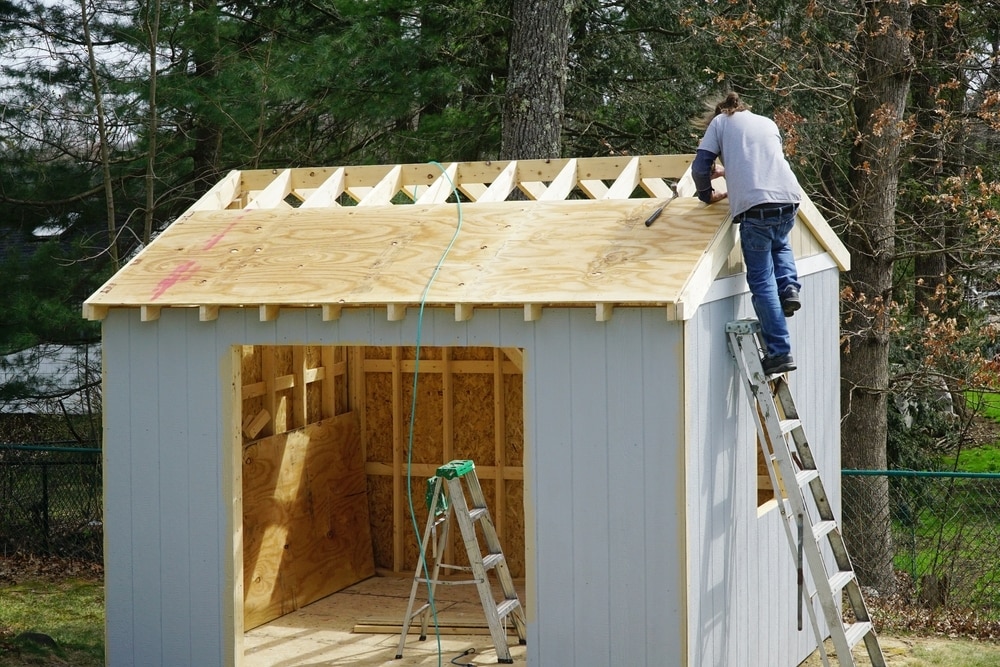 Worker building shed roof in backyard.