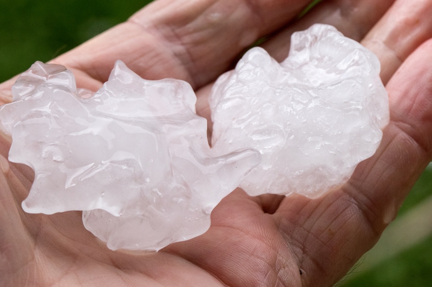 Close-up of hail impacting dark shingles.