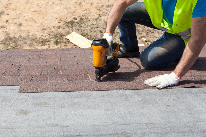 Man using nail gun to apply asphalt shingles to a roof