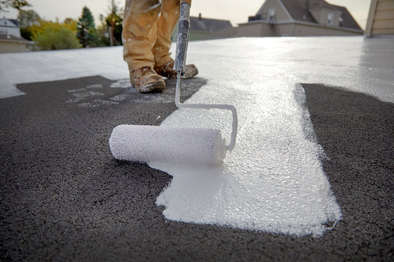 A roofer applies a silicone roof coating