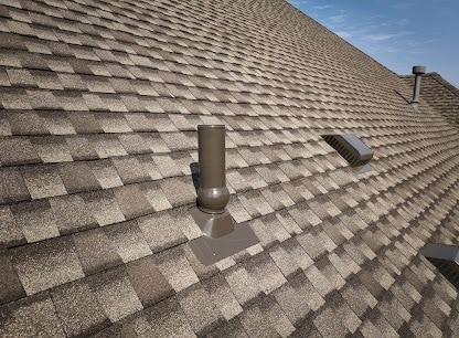 Side view of a metal chimney exhaust on asphalt roof with a cap