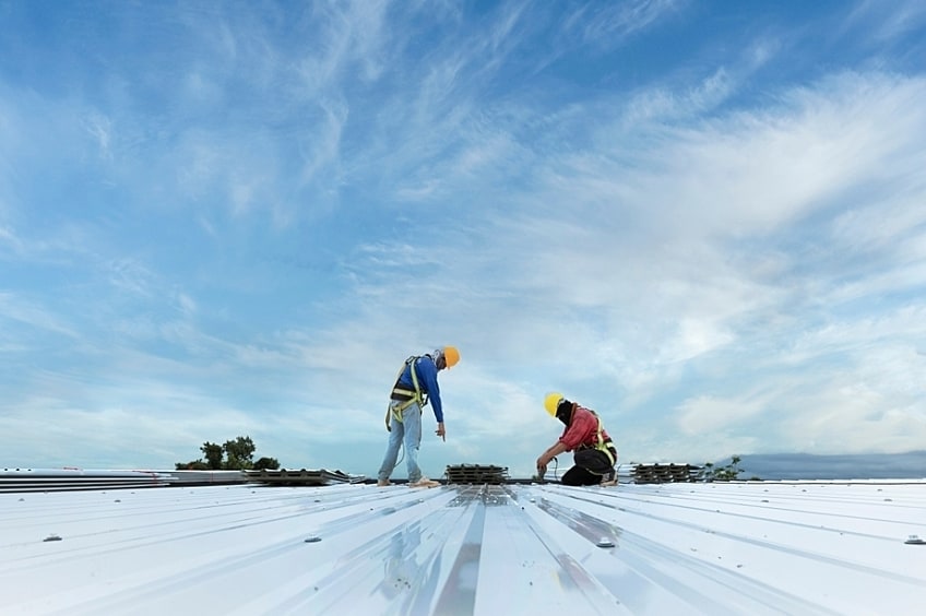 Commercial roofers wearing hardhats use power tools on the roof a building.