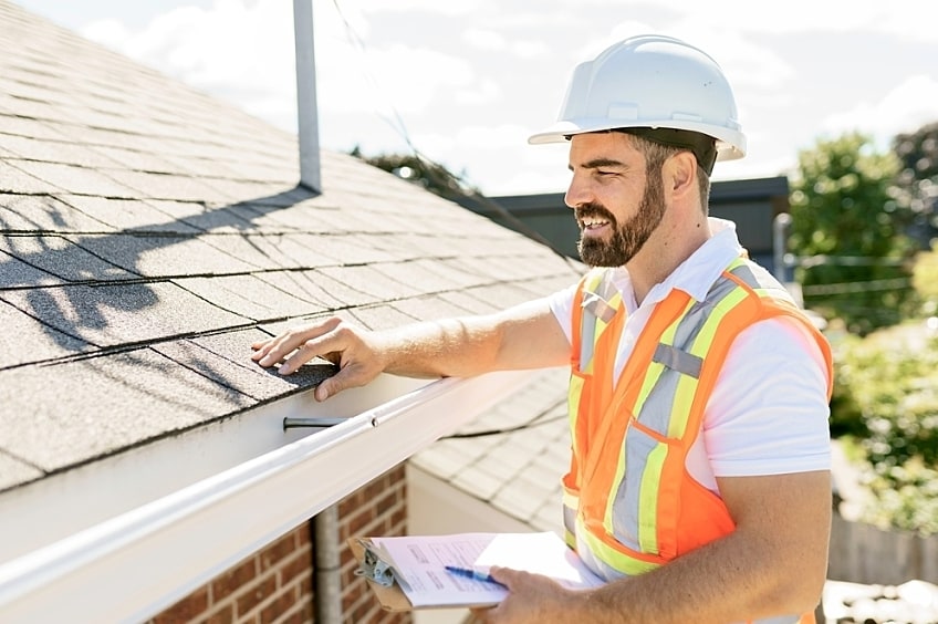 A roofing professional on a ladder inspecting an older roof.