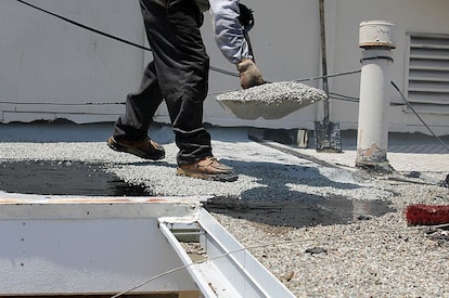 A roofer shovels gravel.
